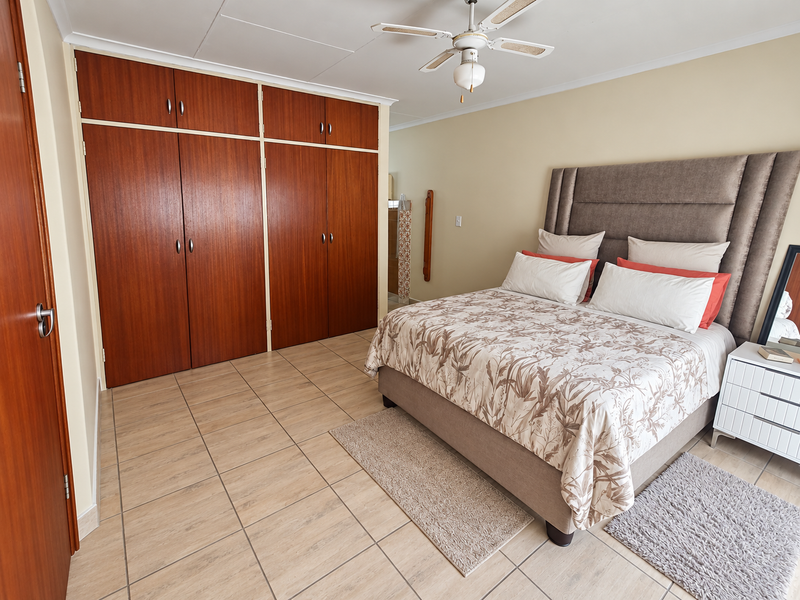 A well-maintained bedroom featuring tiled flooring, a ceiling fan, and extensive built-in wooden cupboards for storage.