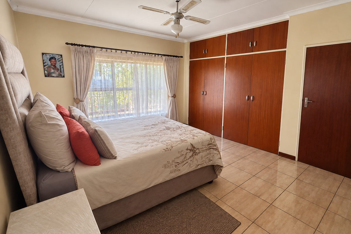 A well-maintained bedroom featuring built-in wooden cupboards, tiled flooring, and a ceiling fan, offering a functional and comfortable living space.
