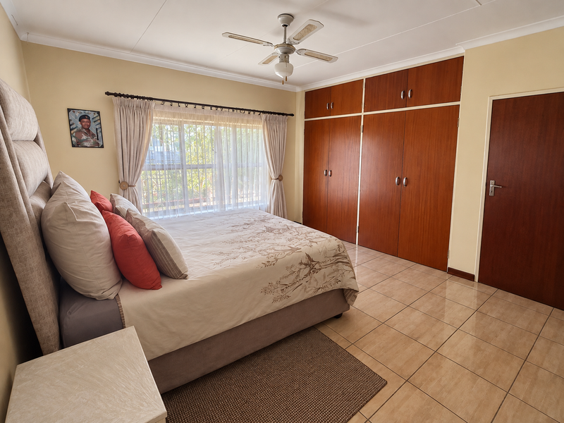 A well-maintained bedroom featuring built-in wooden cupboards, tiled flooring, and a ceiling fan, offering a functional and comfortable living space.