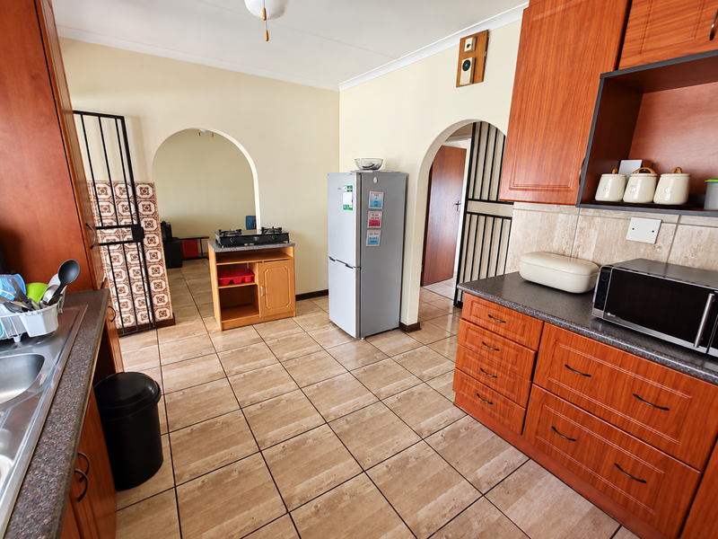 A functional kitchen featuring wood-look laminate cabinetry, tiled flooring, and a tiled backsplash, connected to adjacent living spaces via arched doorways.