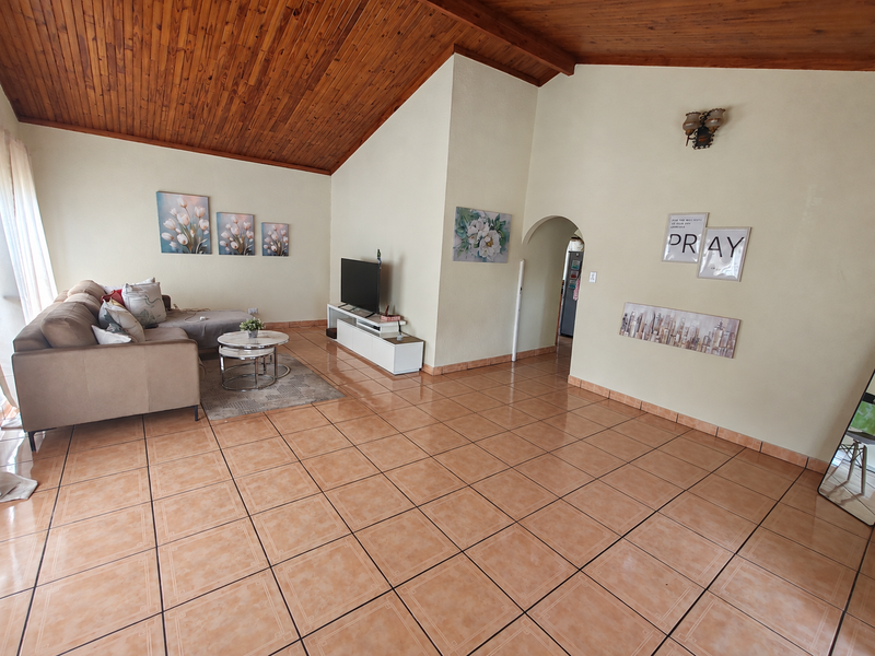 Spacious living room featuring a vaulted timber ceiling, ceramic tiled flooring, and an arched doorway leading to adjacent areas.