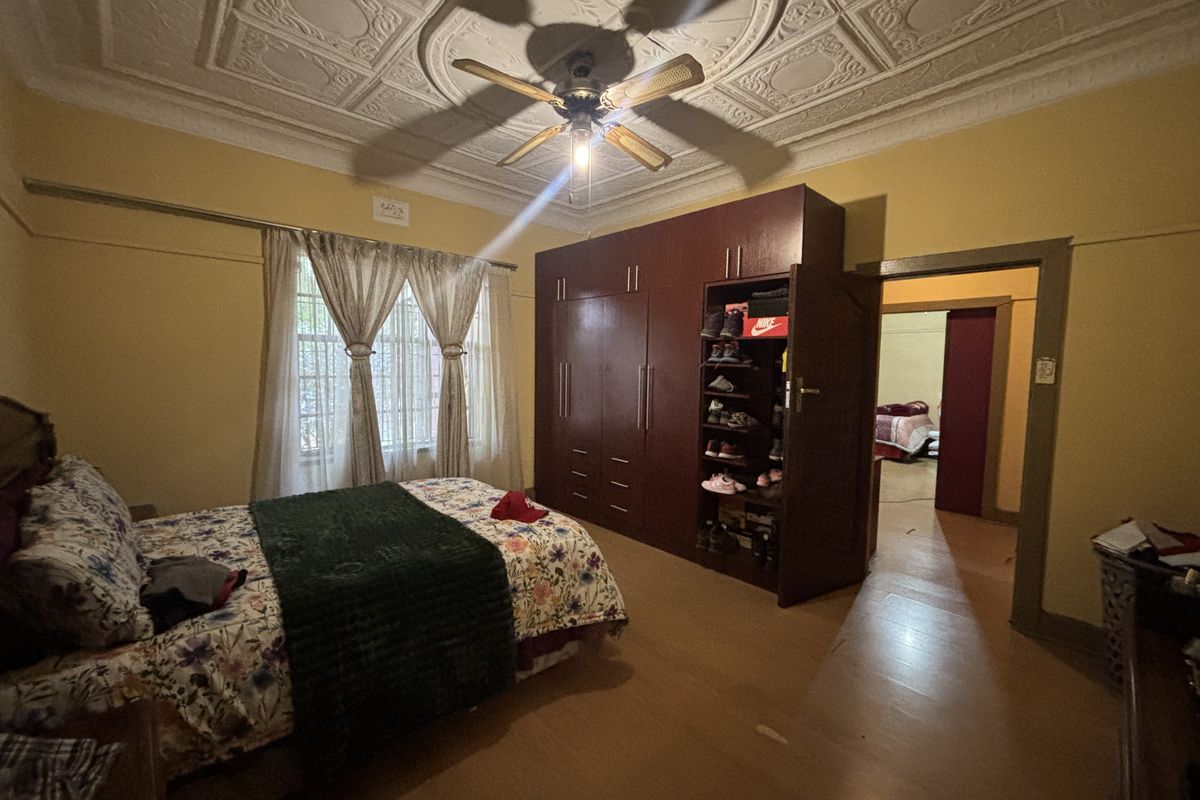 Spacious bedroom featuring an ornate pressed metal ceiling, ceiling fan, built-in wardrobe, and timber flooring.