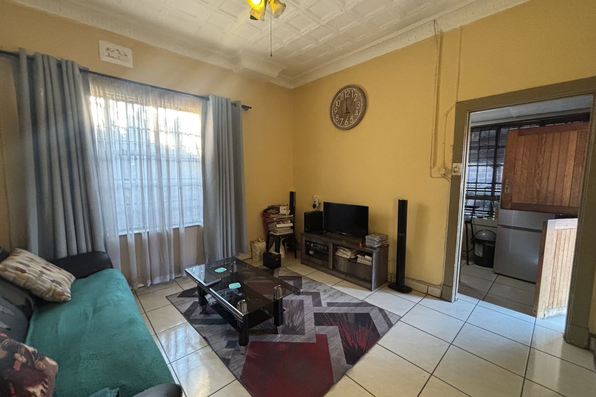A living room featuring tiled flooring and a classic pressed metal ceiling, offering a dated aesthetic with potential for modernization.