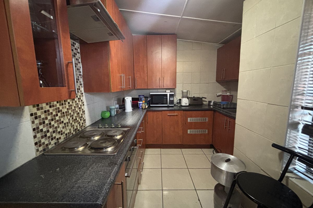 A functional kitchen featuring wood-finish cabinetry, granite countertops, a built-in electric hob with extractor fan, and tiled flooring.