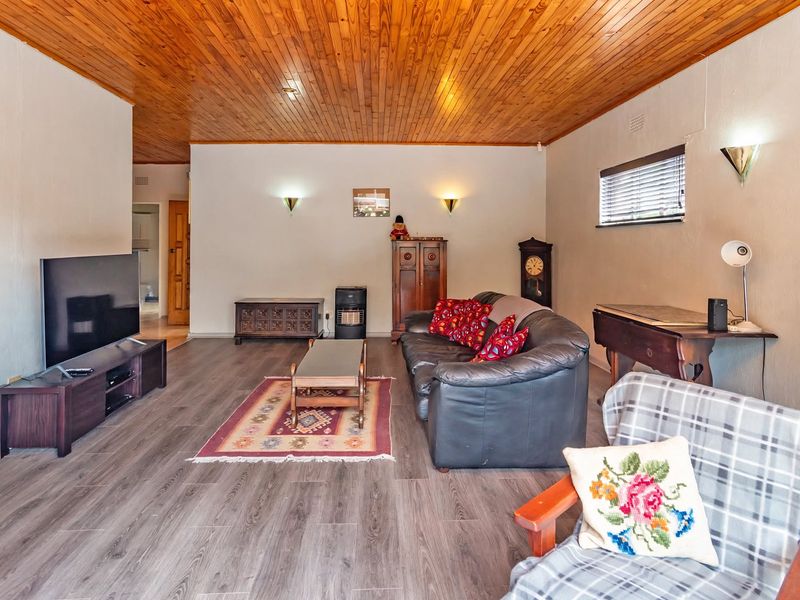 Spacious living room featuring a warm timber tongue and groove ceiling, modern laminate flooring, and wall-mounted lighting fixtures.