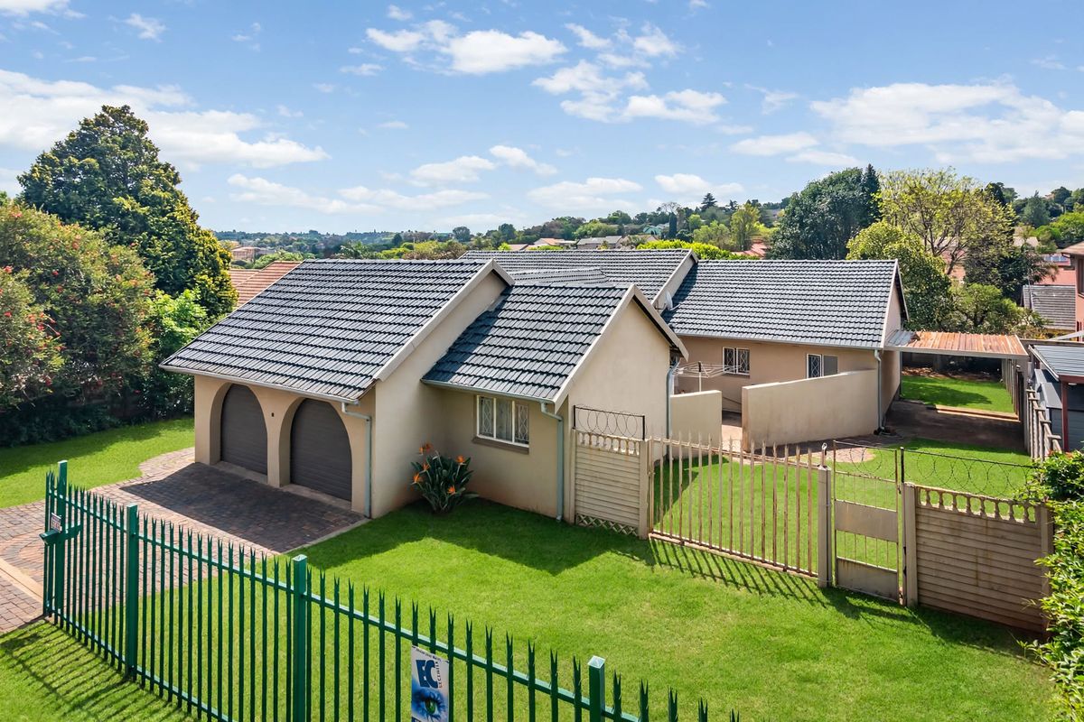 Aerial view of a residential property featuring a double garage, tiled roof, paved driveway, and secure perimeter fencing with a well-maintained lawn.