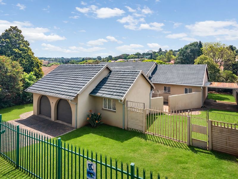 Aerial view of a residential property featuring a double garage, tiled roof, paved driveway, and secure perimeter fencing with a well-maintained lawn.