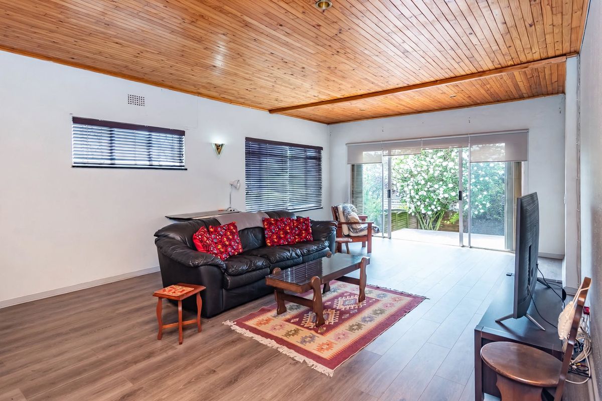 Spacious living room featuring a warm timber tongue and groove ceiling, modern laminate flooring, and large sliding glass doors opening to the garden.