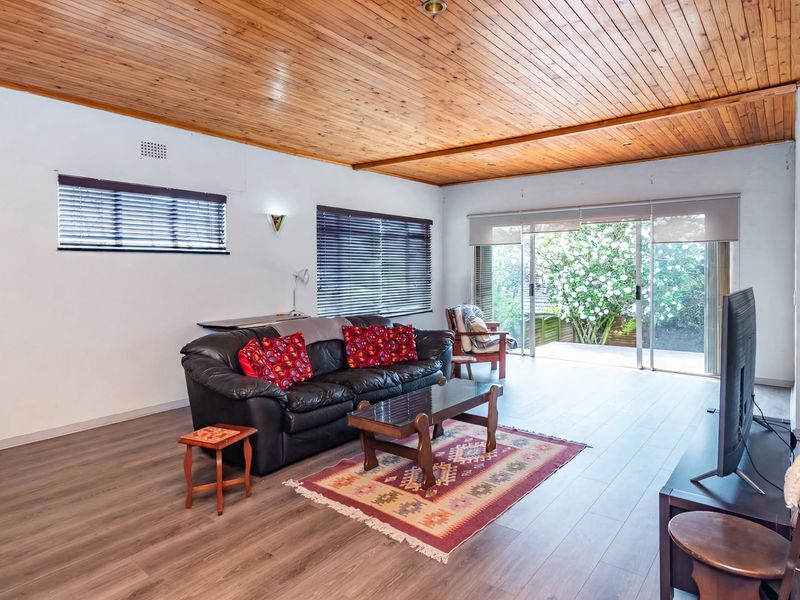 Spacious living room featuring a warm timber tongue and groove ceiling, modern laminate flooring, and large sliding glass doors opening to the garden.