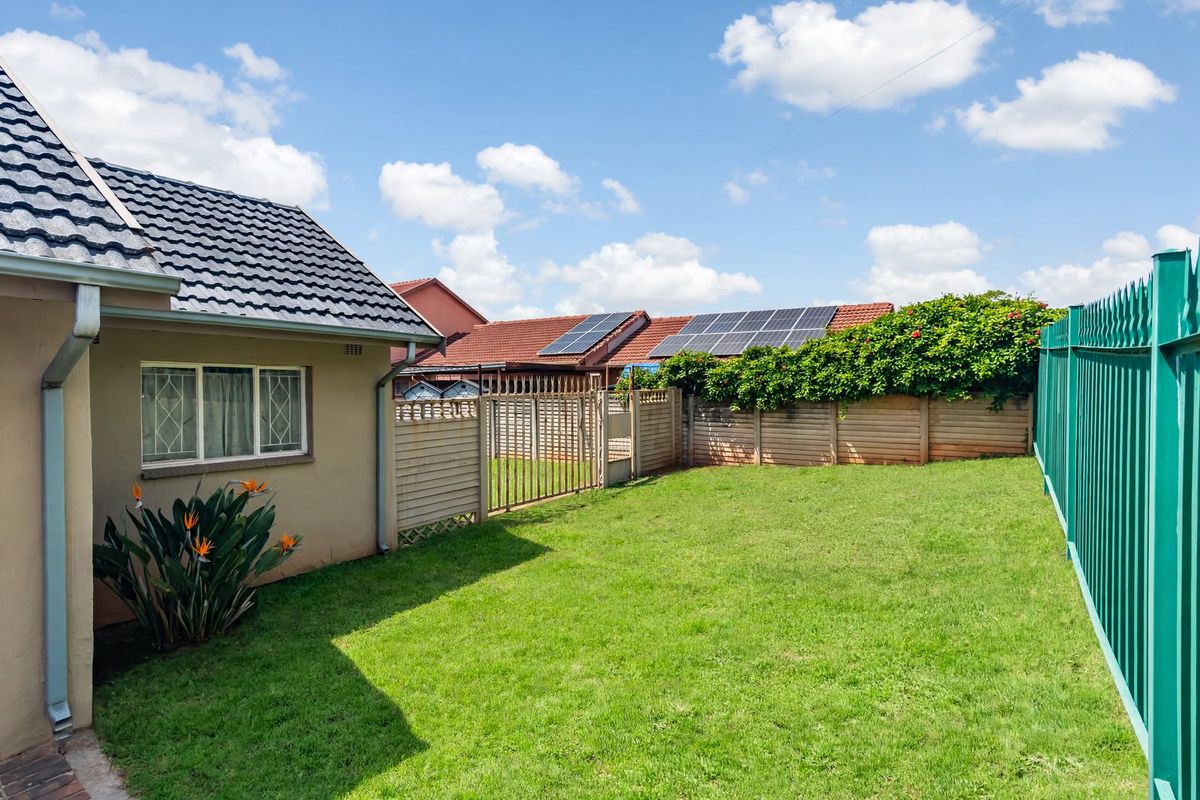 A well-maintained rear garden area featuring a lawn, secure perimeter fencing, and a tiled roof structure with integrated gutters.