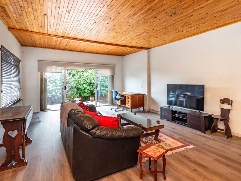 Spacious living room featuring timber tongue and groove ceilings, laminate flooring, and large sliding glass doors providing direct access to the garden area.