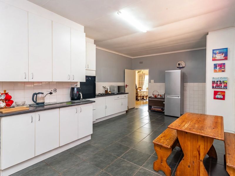 A functional kitchen featuring white built-in cabinetry, dark laminate countertops, ceramic tile backsplash, and dark floor tiles with a dining area.