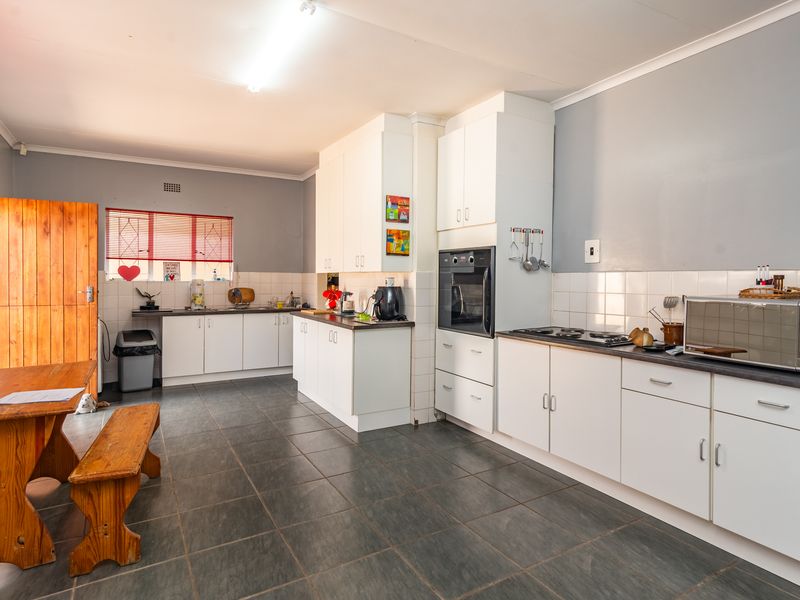 Spacious kitchen featuring white built-in cabinetry, tiled backsplash, integrated oven, and hob, with dark floor tiles and direct access to an outdoor area.