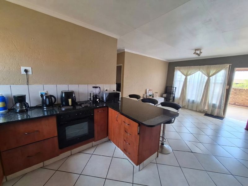 Open plan kitchen and living area featuring granite countertops, wooden cabinetry, built-in oven, and tiled flooring with direct access to an outdoor patio.
