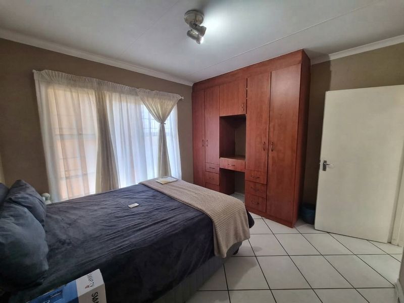 A bedroom featuring tiled flooring, a built-in wooden wardrobe with integrated vanity space, and a ceiling light fixture.