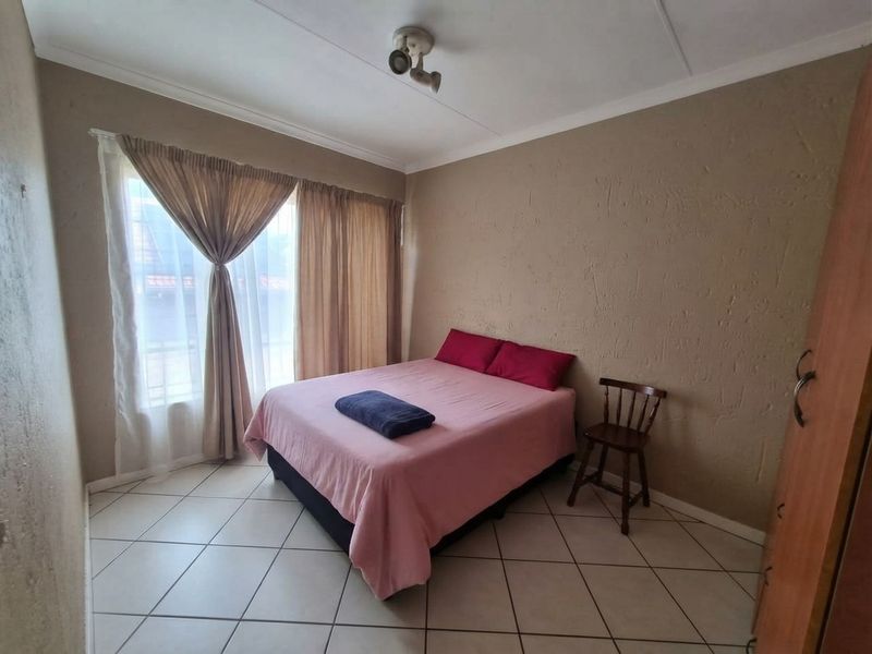 A functional bedroom featuring tiled flooring, neutral textured walls, and a large window with curtain rails.