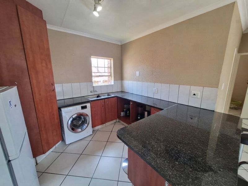 A functional kitchen featuring granite countertops, built-in wooden cabinetry, tiled flooring, and a tiled backsplash, providing a practical workspace for daily needs.