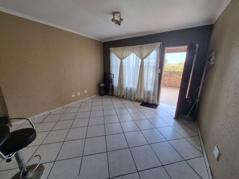 An empty living room featuring tiled flooring, neutral wall tones, and direct access to an outdoor patio area through a sliding glass door.