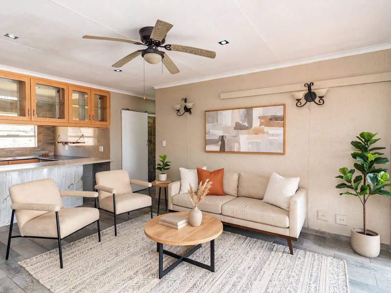 An open-plan living area featuring a kitchen with wooden cabinetry, a marble-look breakfast bar, tiled floors, and a ceiling fan.