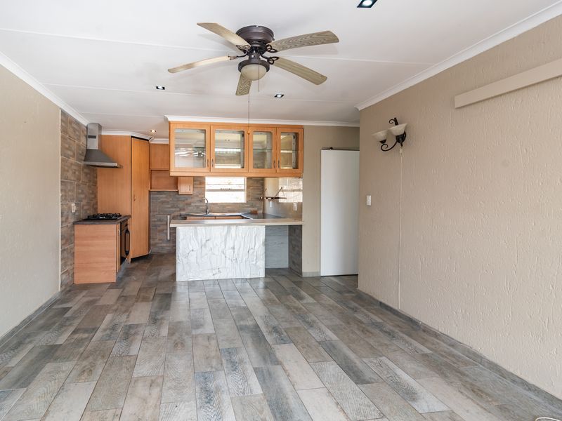 Open-plan kitchen and living area featuring wood-look tiled flooring, built-in cabinetry, a gas hob, and a stone-finished breakfast counter.