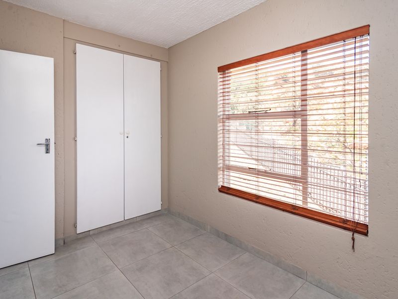 A clean, empty bedroom featuring neutral wall tones, tiled flooring, and built-in cupboards, offering a versatile space ready for personalization.