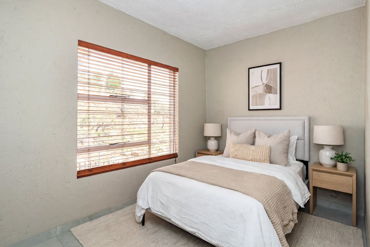 A well-maintained bedroom featuring textured walls and wooden venetian blinds, providing a neutral and comfortable living space.