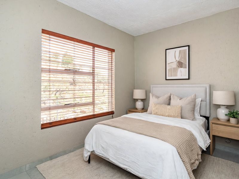 A well-maintained bedroom featuring textured walls and wooden venetian blinds, providing a neutral and comfortable living space.