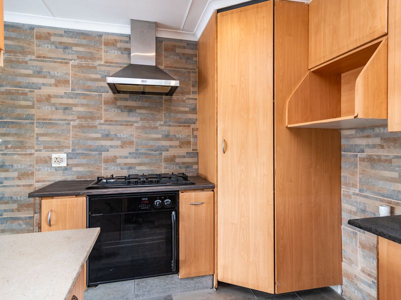 A functional kitchen featuring light wood cabinetry, a gas hob with extractor fan, and decorative stone-look tiled splashbacks.