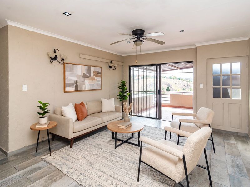 A well-lit living room featuring tiled flooring, a ceiling fan, and sliding glass doors that open onto a balcony with scenic views.