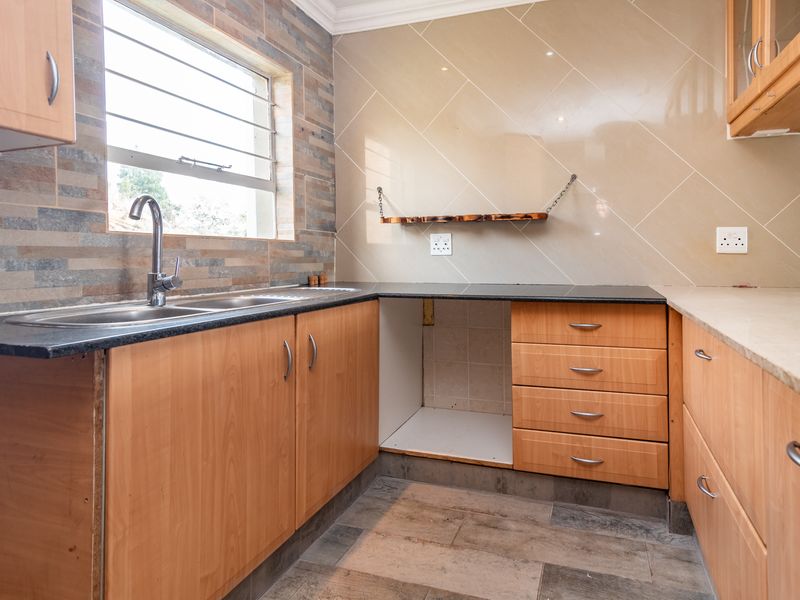 A functional kitchen featuring wood-look cabinetry, granite countertops, a stainless steel sink, and decorative tiled backsplash with space for an under-counter appliance.