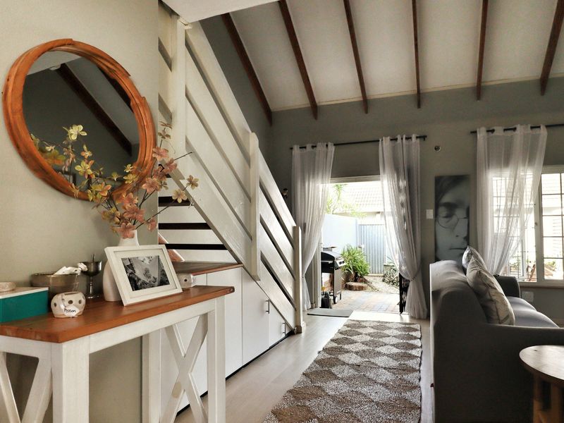 Bright living area featuring exposed timber ceiling beams, a staircase with integrated under-stair storage, and direct access to an outdoor patio area.