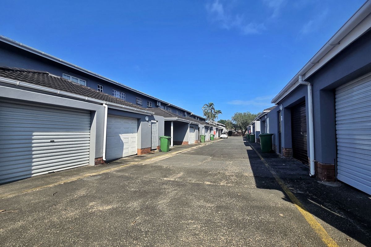 A view of the rear driveway area featuring multiple garage units with roller doors and paved access.