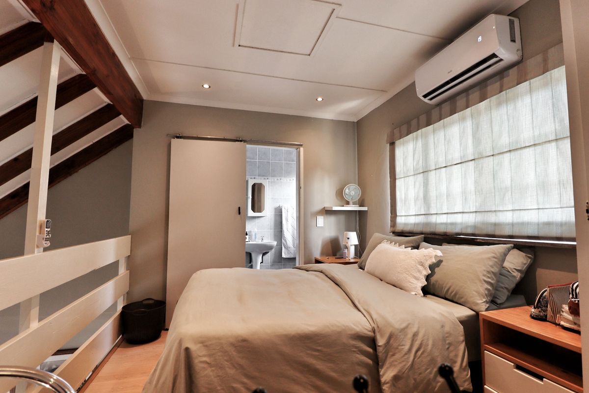 A well-maintained bedroom featuring exposed timber beams, split-system air conditioning, and direct access to an en-suite bathroom.