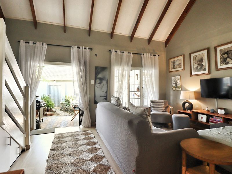 Spacious living room featuring a high vaulted ceiling with exposed timber beams, laminate flooring, and direct access to an outdoor patio area.