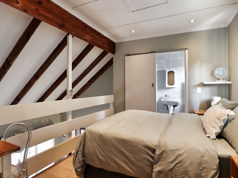 A loft-style bedroom featuring exposed timber rafters, a timber balustrade, and an en-suite bathroom with a pedestal basin.