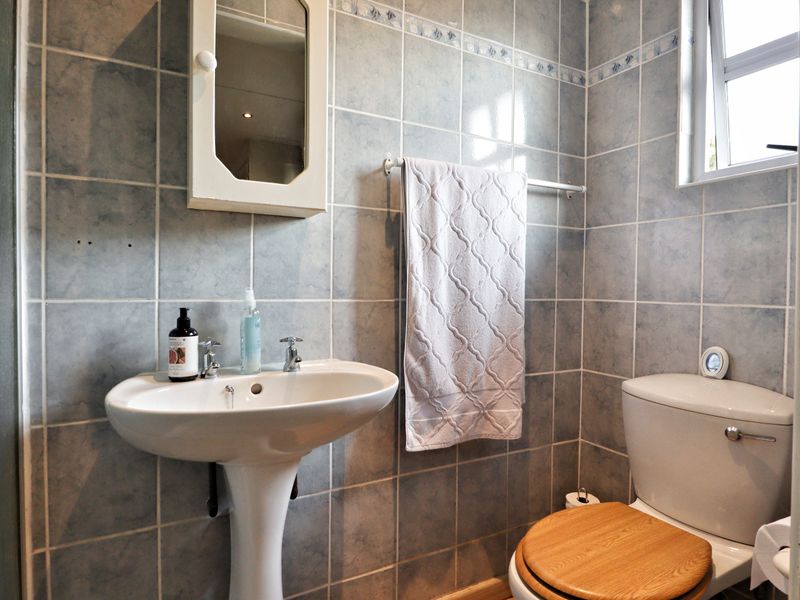 A functional bathroom featuring tiled walls, a pedestal basin, a toilet, and a wall-mounted medicine cabinet with natural light from a side window.