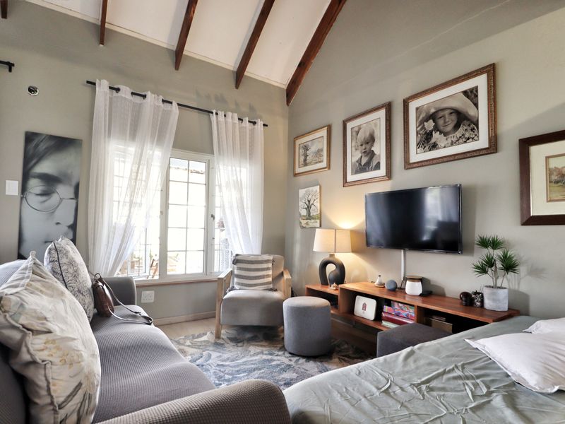 A cozy living room featuring a vaulted ceiling with exposed timber beams and a large multi-pane window providing natural light.
