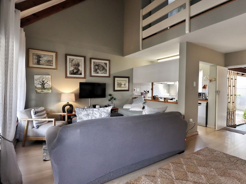 Open-plan living area featuring a double-volume vaulted ceiling with exposed timber beams, a mezzanine level, and a convenient kitchen pass-through window.