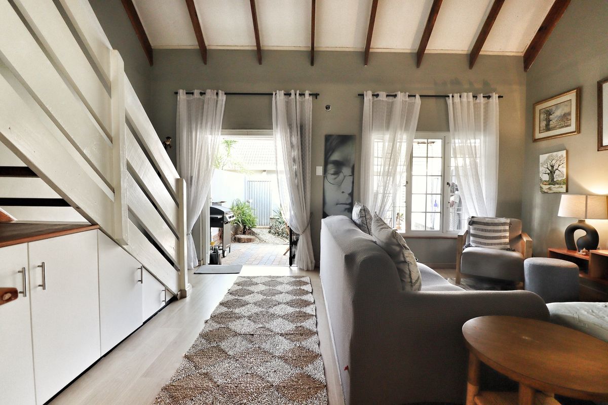 Bright living room featuring exposed timber ceiling beams, laminate flooring, and convenient built-in under-stair storage, with direct access to an outdoor patio area.