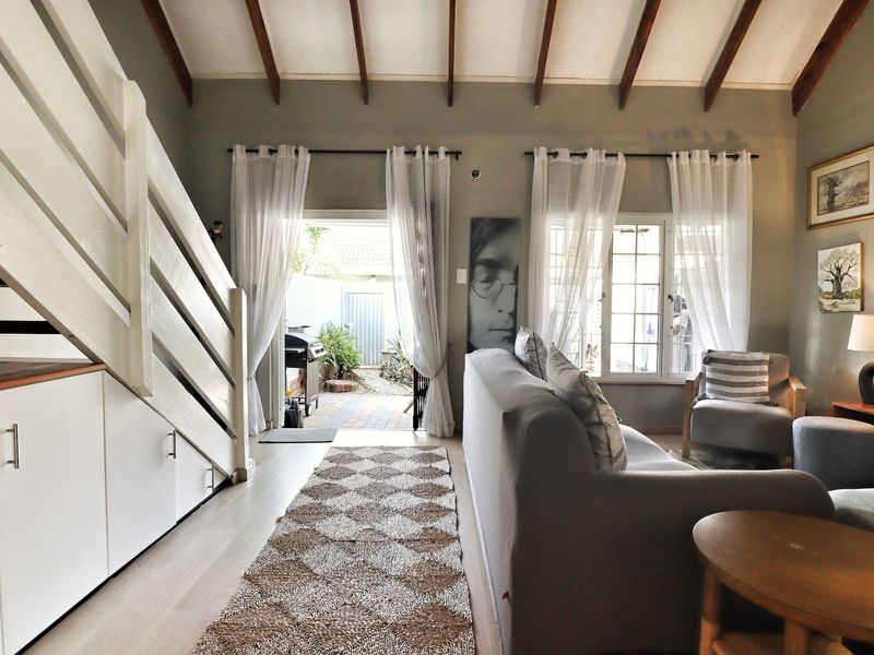 Bright living room featuring exposed timber ceiling beams, laminate flooring, and convenient built-in under-stair storage, with direct access to an outdoor patio area.