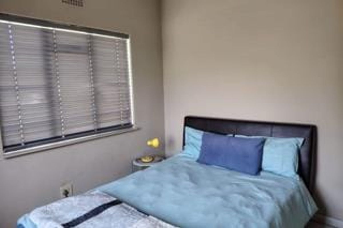 A functional bedroom featuring neutral wall finishes and a window fitted with venetian blinds.