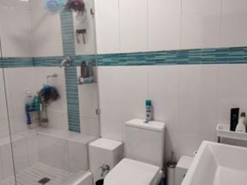 A modern bathroom featuring a glass-enclosed shower with a built-in tiled bench, mosaic accent tiling, and a clean white sanitary ware suite.