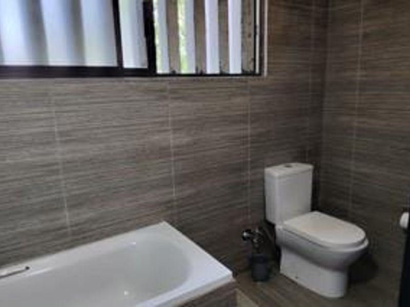 A functional bathroom featuring full-height wall tiling, a standard bathtub, and a modern toilet, complemented by a louvre window for natural ventilation.