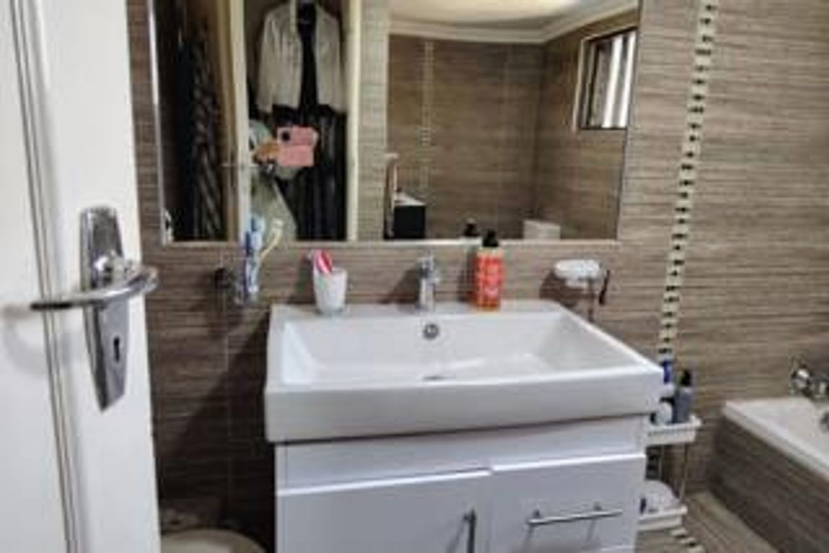 A functional bathroom featuring a modern white vanity with a basin, large wall mirror, and neutral-toned wall tiling.