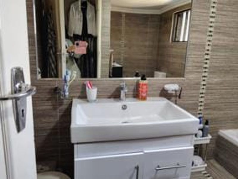A functional bathroom featuring a modern white vanity with a basin, large wall mirror, and neutral-toned wall tiling.