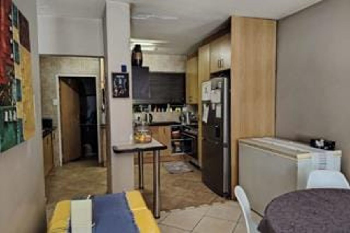 A functional kitchen featuring built-in cabinetry, laminate countertops, and a breakfast bar, seamlessly connected to the dining area with tiled flooring throughout.
