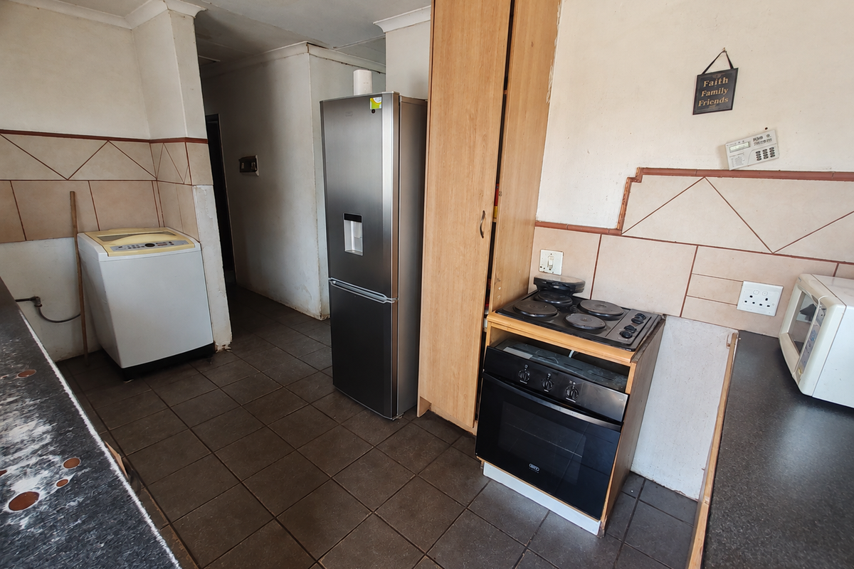 A functional kitchen featuring tiled splashbacks, built-in oven and hob, and dark floor tiles, offering potential for modernization and cosmetic updates.