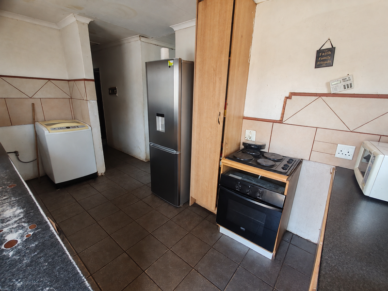 A functional kitchen featuring tiled splashbacks, built-in oven and hob, and dark floor tiles, offering potential for modernization and cosmetic updates.