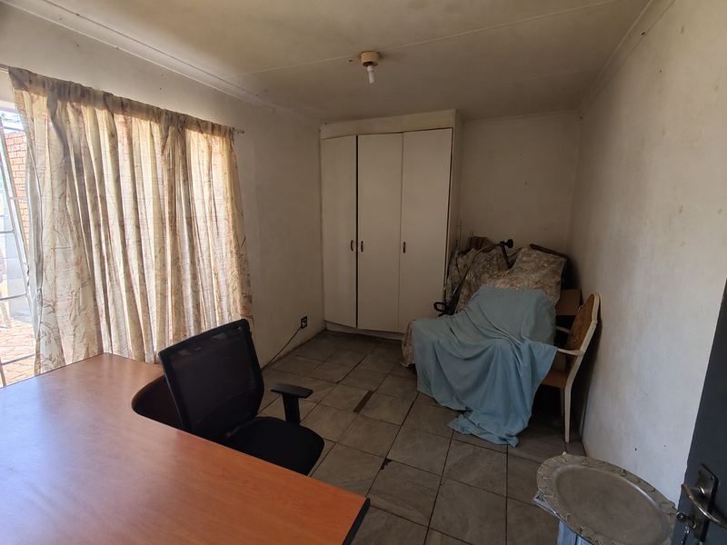 A bedroom featuring tiled flooring and a built-in wardrobe, currently in need of cosmetic updates and wall repairs.