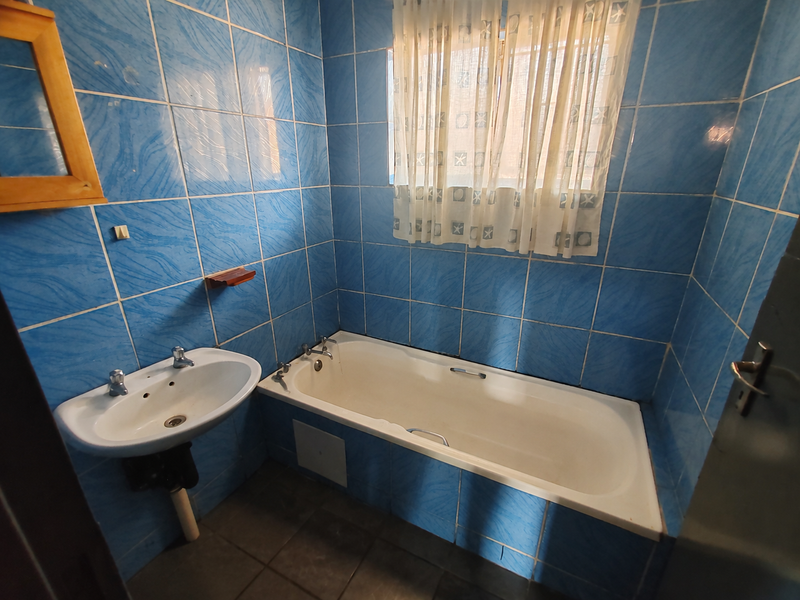 A dated bathroom featuring blue wall tiles, a built-in bathtub, and a wall-mounted basin, offering potential for a modern renovation.